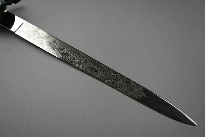 A long silver knife with a design on it

Description automatically generated