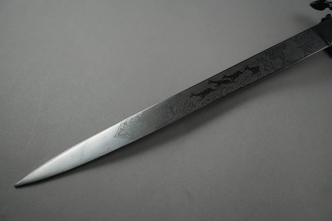 A long silver blade with a design on it

Description automatically generated