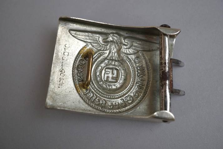A metal belt buckle with a symbol

Description automatically generated