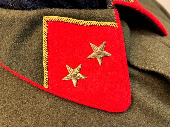 A red patch with gold stars on a green uniform

Description automatically generated