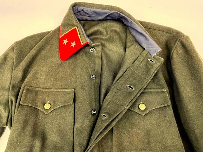 A green military jacket with a red patch on it

Description automatically generated