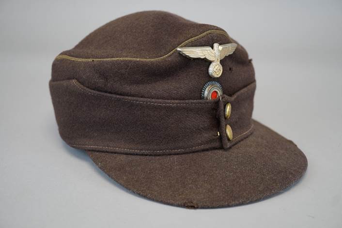 A brown hat with a small metal eagle on it

Description automatically generated